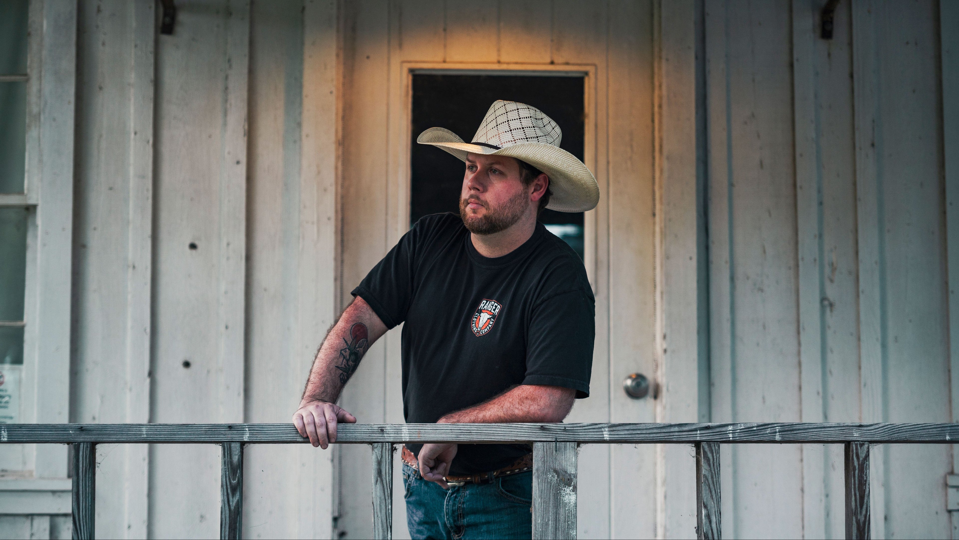 Man wearing a cowboy hat standing on a porch of a wooden building.